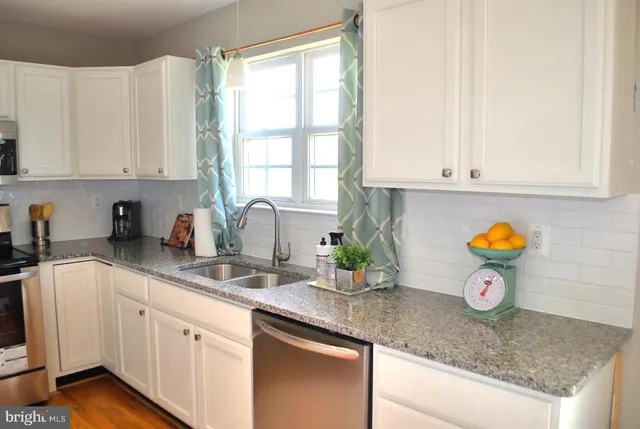 a kitchen with stainless steel appliances granite countertop white cabinets a window and a sink