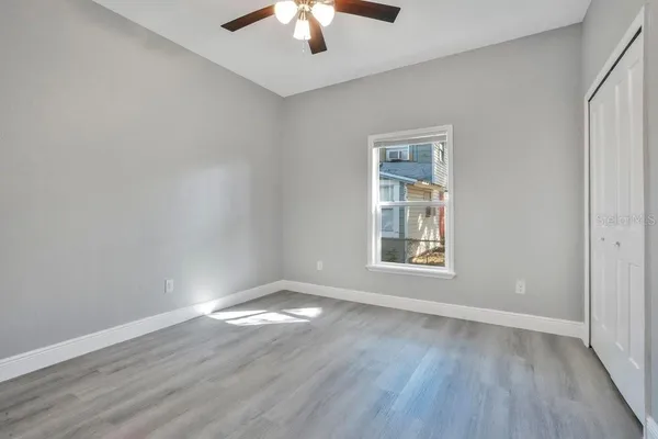 an empty room with wooden floor chandelier fan and windows