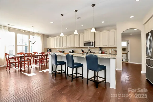 a open kitchen with stainless steel appliances granite countertop a dining table chairs stove a refrigerator and cabinets