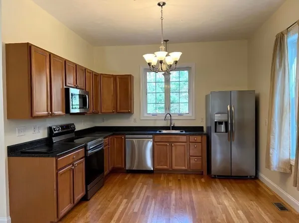 a kitchen with stainless steel appliances granite countertop wooden cabinets a refrigerator a sink a stove a microwave and island with wooden floor