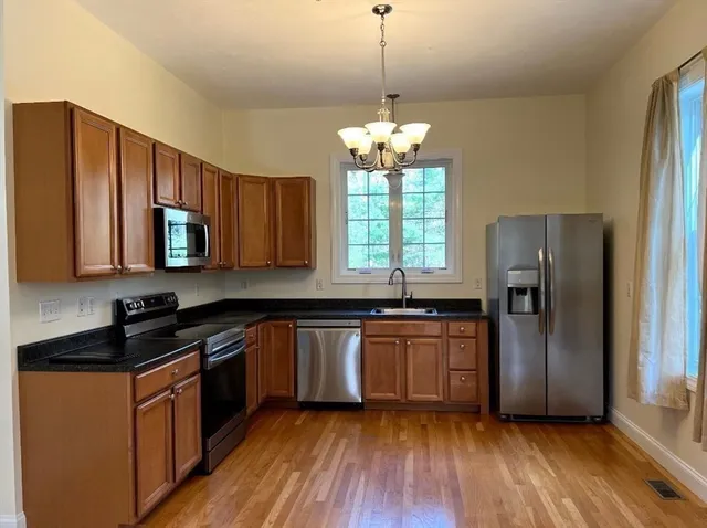 a kitchen with stainless steel appliances granite countertop wooden cabinets a refrigerator a sink a stove a microwave and island with wooden floor