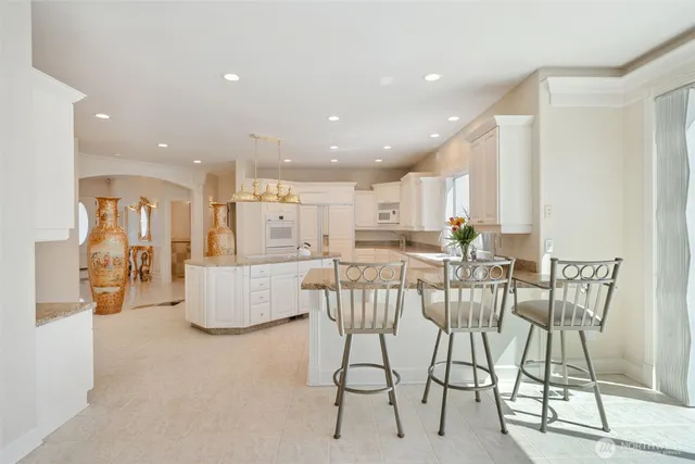 a dining hall with stainless steel appliances kitchen island granite countertop a dining table chairs and a refrigerator