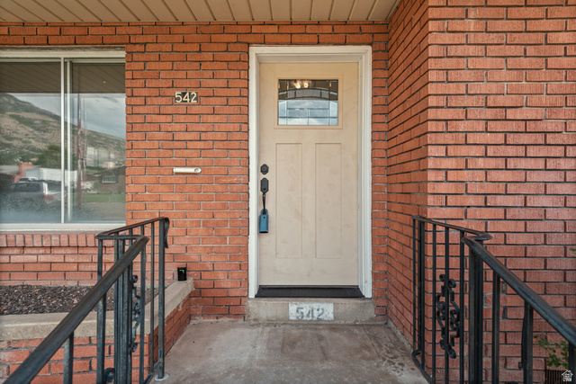542 East 3400th Street North Provo, UT 84604 - Photo 7 of 39 Red brick exterior featuring a cream-colored entry door with decorative glass panel, complemented by a black wrought iron railing and a window with a reflective mountain backdrop