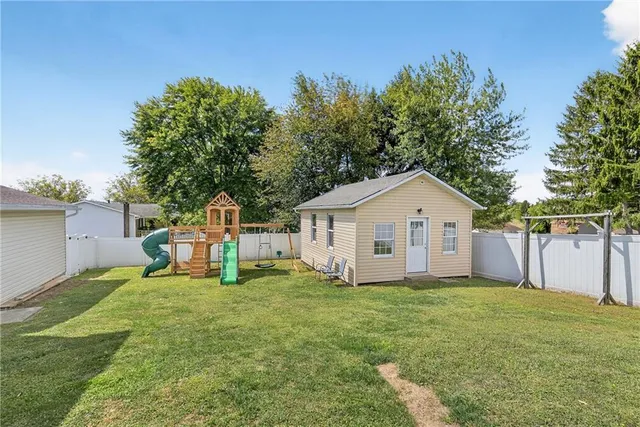 a white house that has a small yard and large trees with wooden fence