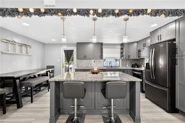 a kitchen with stainless steel appliances a stove a sink a refrigerator and chairs