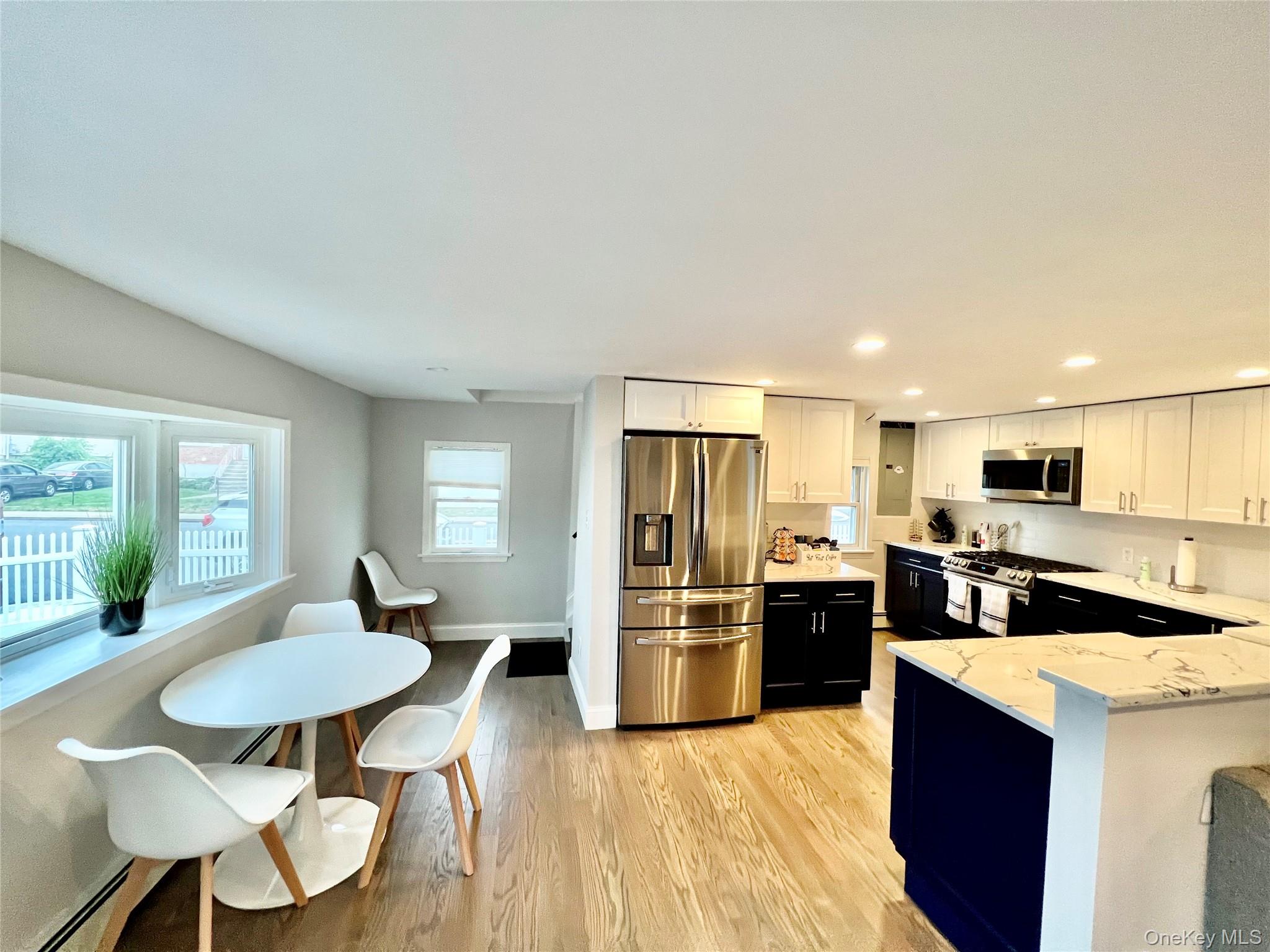 100 Clubhouse Road Bellmore, NY 11710 - Photo 6 of 18 Kitchen featuring two tone cabinetry, stainless steel appliances, light wood finished floors, light stone counters, and a peninsula