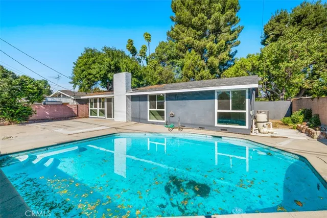 a white house that has a big pool with a yard and a large tree
