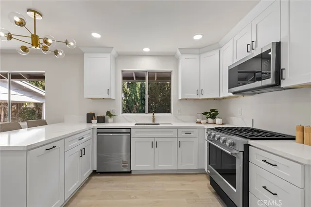 a kitchen with stainless steel appliances granite countertop white cabinets a sink dishwasher and a stove top oven with wooden floor