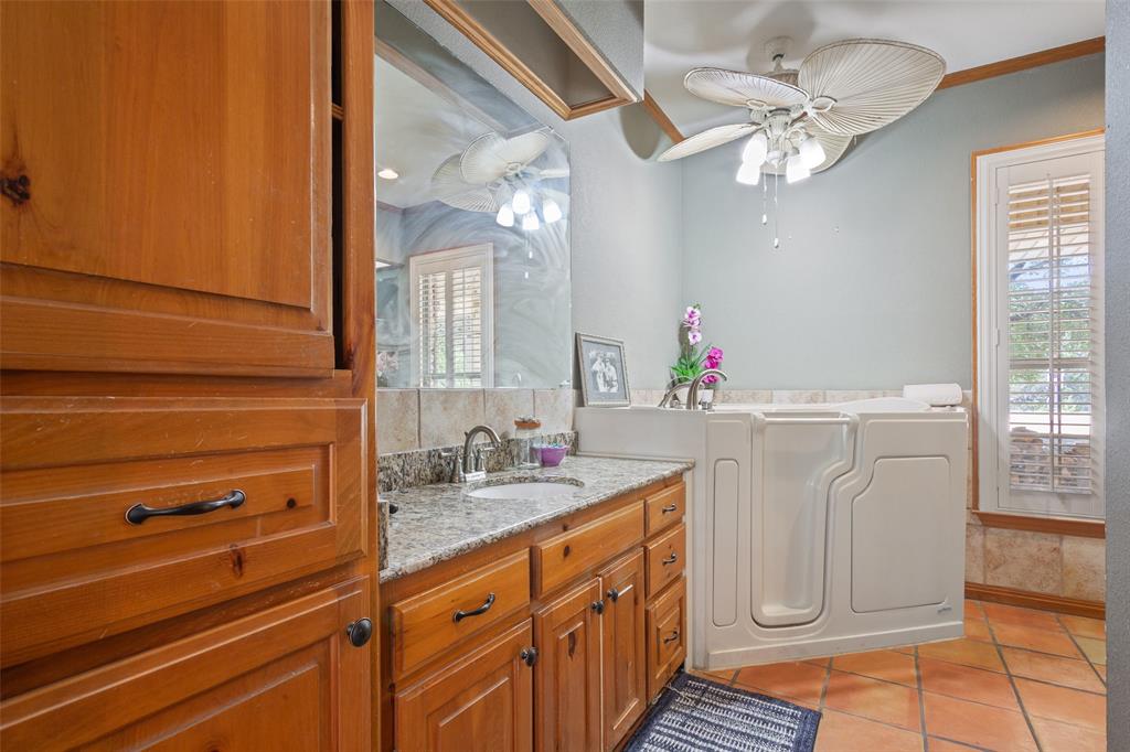 564 Sam Bass Road McGregor, TX 76657 - Photo 16 of 37 Bathroom featuring a walk-in bathtub, dual vanity with granite countertop, wood-finish cabinetry, and terracotta-style floor tiles
