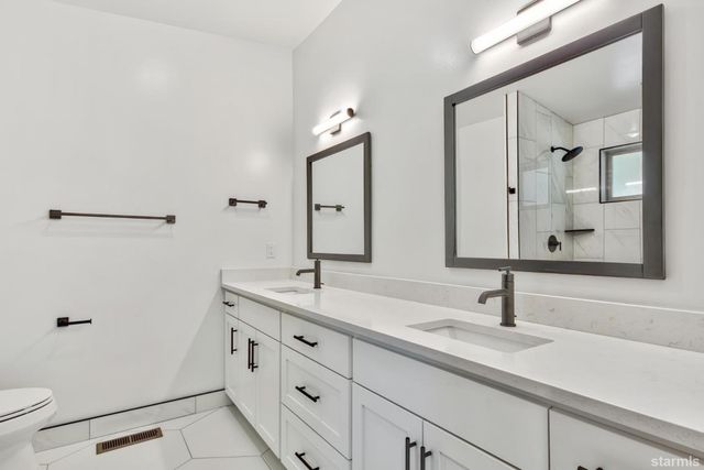 a bathroom with a double vanity sink and mirror with toilet