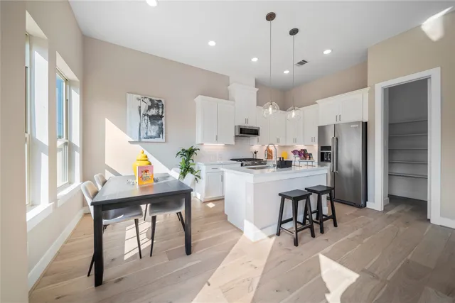a kitchen with stainless steel appliances kitchen island granite countertop a refrigerator a stove a sink a dining table and chairs with wooden floor
