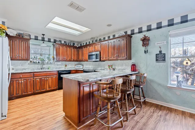 a kitchen with stainless steel appliances granite countertop a kitchen island a stove a sink dishwasher and cabinets with wooden floor