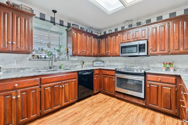 a kitchen with stainless steel appliances granite countertop wooden cabinets a stove top oven a sink and dishwasher a oven with wooden floor