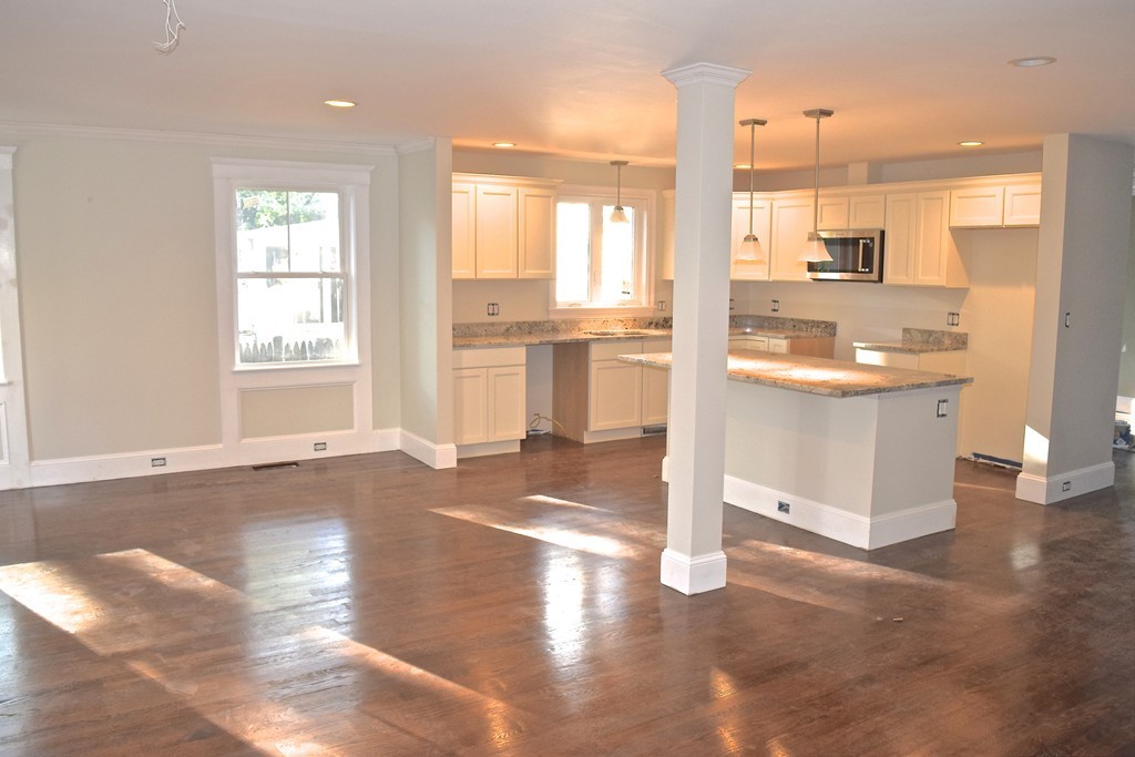 a view of a kitchen with kitchen island granite countertop wooden floors and a view of living room
