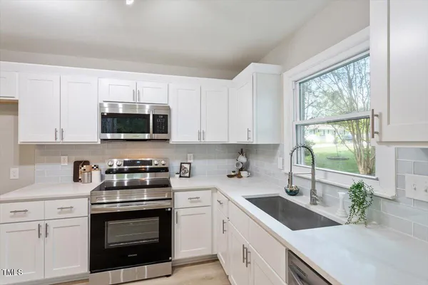 a kitchen with stainless steel appliances granite countertop white cabinets a sink a stove a microwave and view