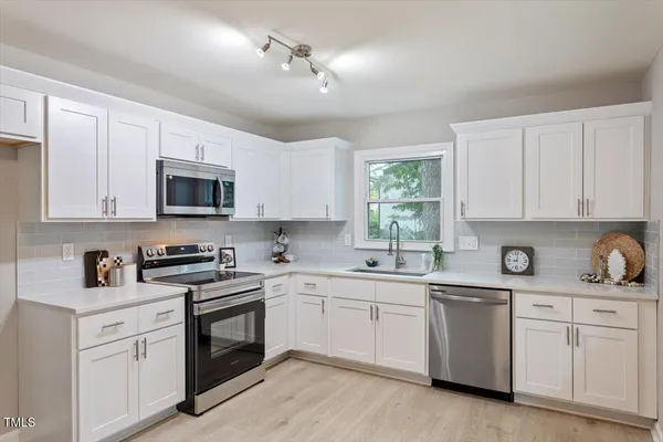 a kitchen with white cabinets appliances a sink and a window