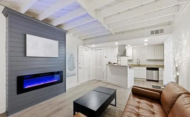 a living room with stainless steel appliances furniture a fireplace and a kitchen view