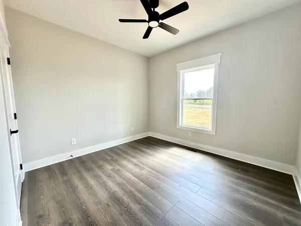 an empty room with wooden floor fan and windows