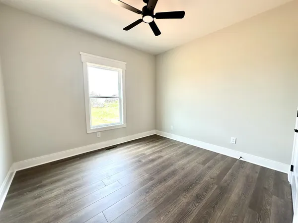 an empty room with wooden floor ceiling fan and windows