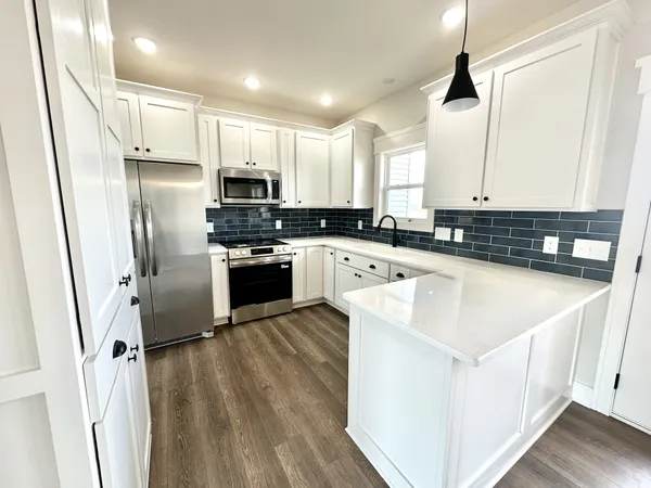 a kitchen with stainless steel appliances granite countertop a sink a stove a refrigerator with white cabinets and wooden floor