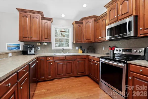 a kitchen with stainless steel appliances granite countertop a sink dishwasher stove and wooden cabinets with wooden floor