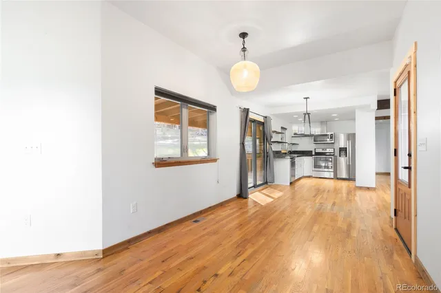 a view of empty room with wooden floor and kitchen view