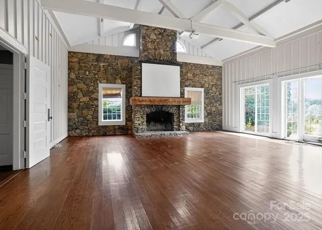 an empty room with wooden floor fireplace and windows