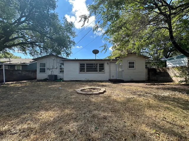 a backyard of a house with wooden fence and a large tree