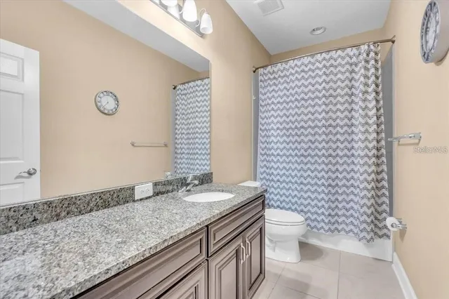 a bathroom with a granite countertop sink a toilet a mirror and shower curtain