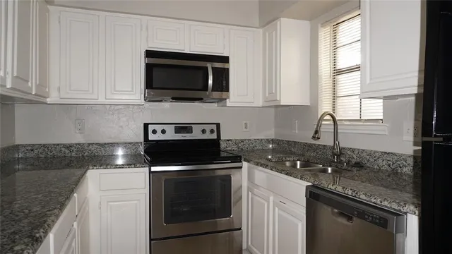 a kitchen with granite countertop white cabinets appliances and a window