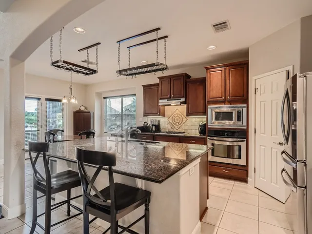 a kitchen with stainless steel appliances granite countertop a stove a refrigerator a kitchen island a table and chairs