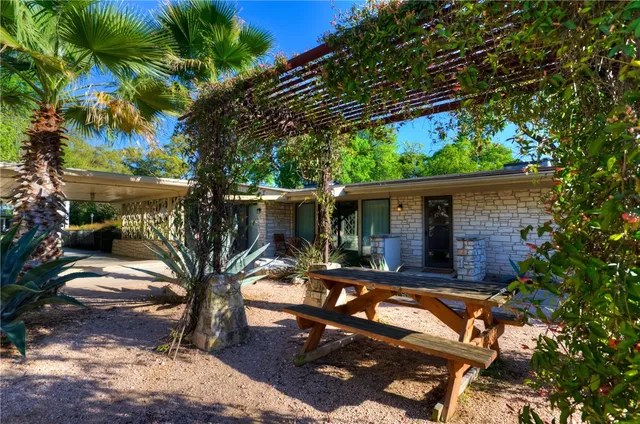 a backyard of a house with table and chairs potted plants and large tree