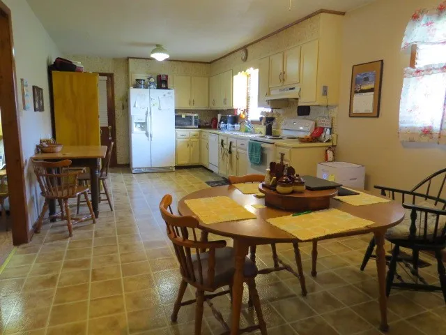 a kitchen with stainless steel appliances kitchen island granite countertop a dining table chairs and a refrigerator