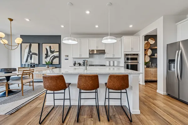 a kitchen with stainless steel appliances kitchen island granite countertop a refrigerator a stove a sink and chairs with wooden floor