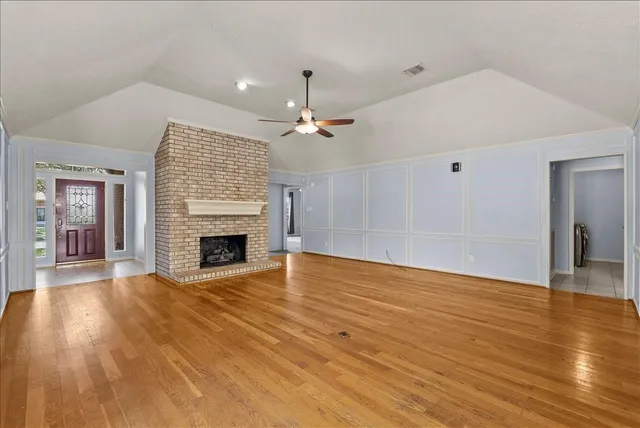 a view of an empty room with wooden floor fireplace and a window
