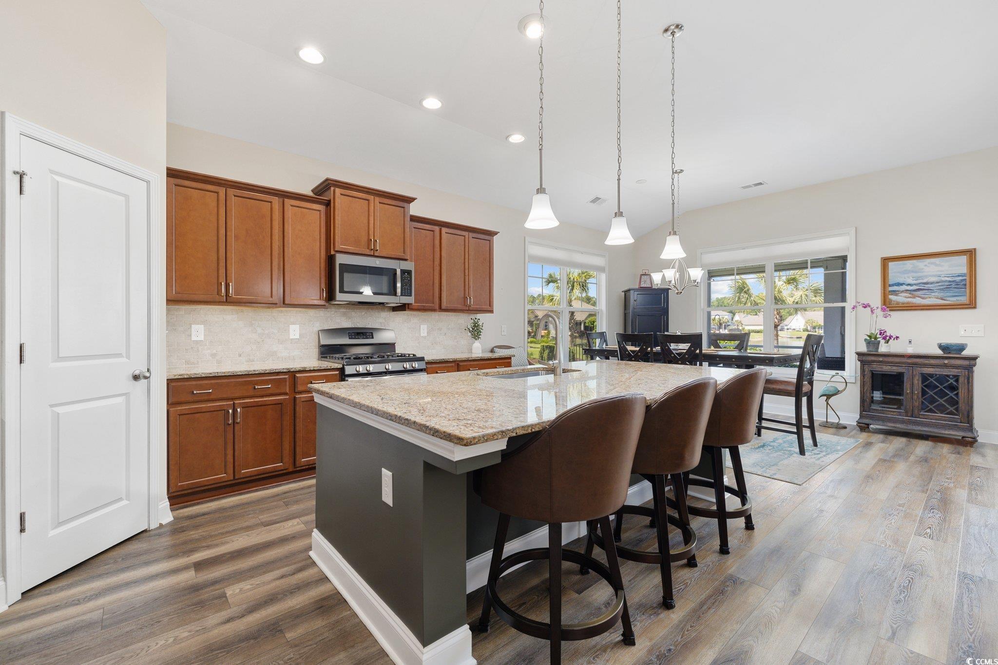 179 Hyacinth Loop Murrells Inlet, SC 29576 - Photo 6 of 40 Kitchen featuring wood finished floors, a kitchen breakfast bar, brown cabinets, a sink, and stainless steel appliances