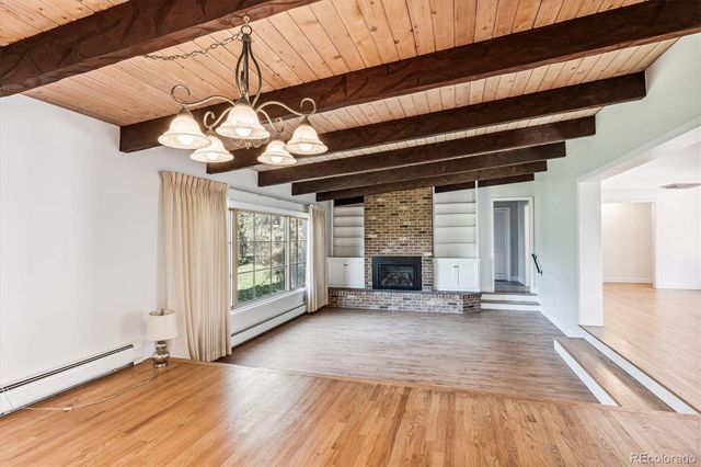 a view of an empty room with wooden floor a fireplace and a window