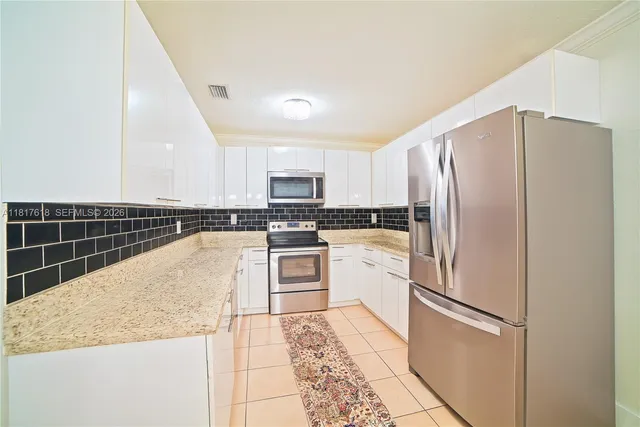 a kitchen with granite countertop a refrigerator and white cabinets