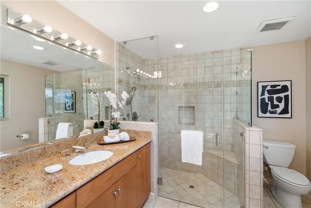 a bathroom with a granite countertop sink a toilet a mirror a vanity and shower