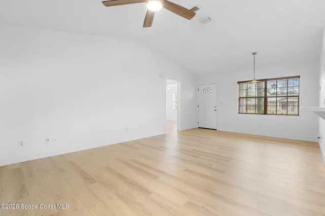an empty room with chandelier fan and windows