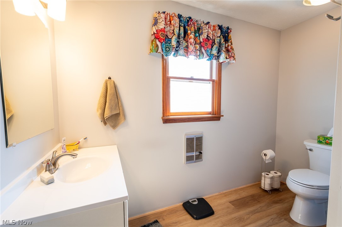 14027 Mayfield Road Huntsburg, OH 44046 - Photo 23 of 50 Bathroom featuring a single-pane window with wood trim, wood-finish flooring, a white vanity with an integrated sink, a wall-mounted mirror, and a white toilet