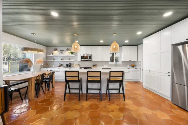 a kitchen with stainless steel appliances kitchen island granite countertop a dining table chairs sink and cabinets