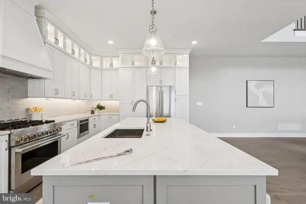 a large white kitchen has a stove a sink a refrigerator and white cabinets with wooden floor