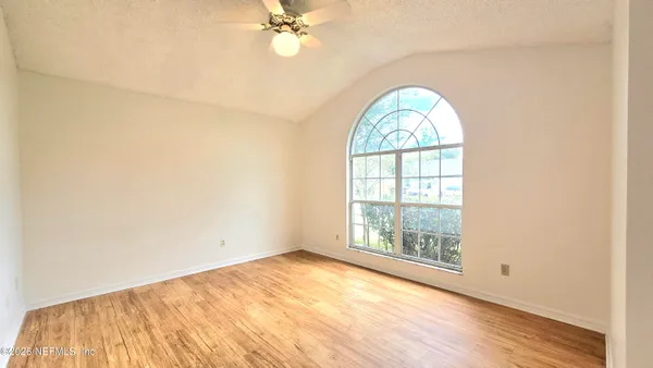 an empty room with wooden floor fan and windows