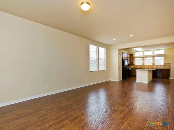 a view of empty room with wooden floor and kitchen view
