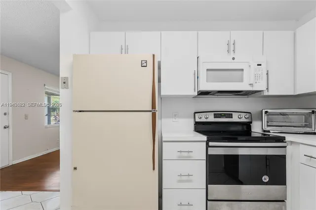 a white refrigerator freezer and a stove sitting inside of a kitchen with granite countertop white cabinets