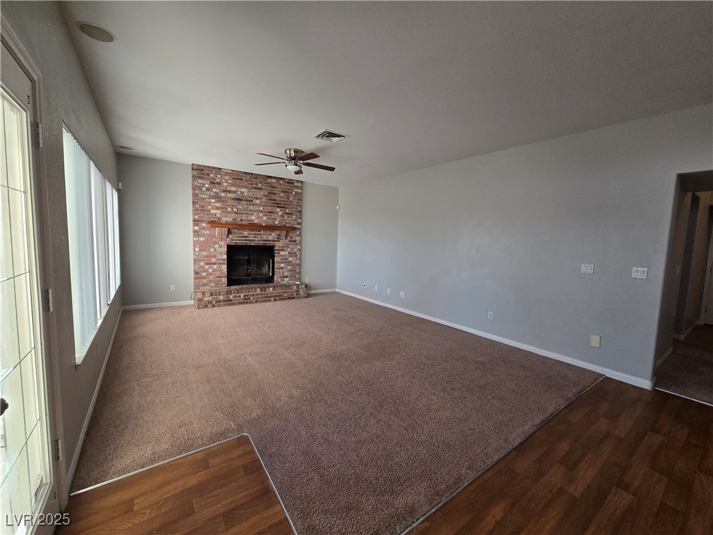 Undisclosed Address Las Vegas, NV 89149 - Photo 9 of 34 Unfurnished living room featuring a ceiling fan, dark wood-style floors, a brick fireplace, and dark colored carpet