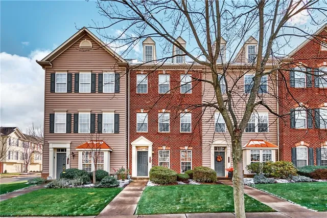 front view of a brick house with a yard and large trees