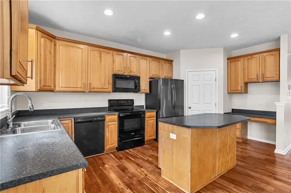 a kitchen with kitchen island granite countertop a stove top oven a sink dishwasher a refrigerator and cabinets with wooden floor