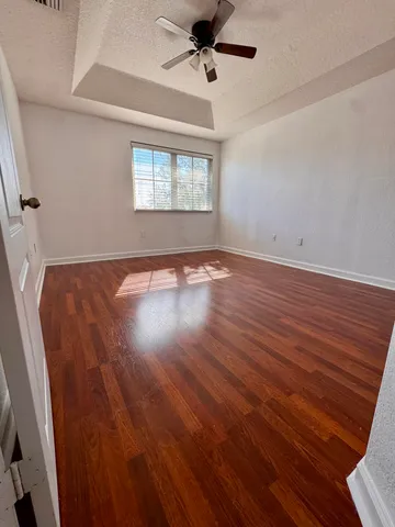 an empty room with wooden floor fan and windows